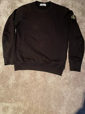 Svart stickad tröja Stone Island - Snygg svart stickad tröja från Stone Island med rund halsringning och ribbade muddar. Tröjan har en diskret Stone Island-logga broderad på bröstet och den klassiska patchen på vänster ärm. Perfekt för dig som gillar streetwear och stilrena plagg.