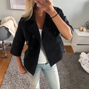 Svart trekvartsärmad dubbelknäppt jacka - Snygg svart kort jacka med dubbelknäppning och krage. Jackan har trekvartsärmar och en klassisk, stilren look som passar perfekt till jeans eller kjol. Materialet känns som bomull eller polyester och modellen är croppad. Storlek s/m💕