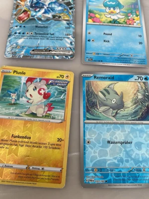 Fyra Pokémonkort med olika motiv - Säljer fyra Pokémonkort med motiv av Plusle, Remoraid och två vattenpokémon. Korten har färgstarka illustrationer och text på både engelska och tyska. Perfekt för samlare eller dig som gillar Pokémon. Materialet är klassiskt glansigt papp.