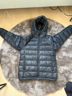 Svart dunjacka från Peak Performance - Säljer en svart dunjacka från Peak Performance med huva och dragkedja framtill. Jackan har två sidofickor med dragkedja och justerbar dragsko i huvan. Perfekt för kalla vinterdagar och riktigt skön att bära. Säljer då den blivit för stor o kan inte användas denna vintern. Den är för stor för mig och är 170 58 kg den är L i barn storlek men jag sätter den som S för den e så stor. Ny pris 3000