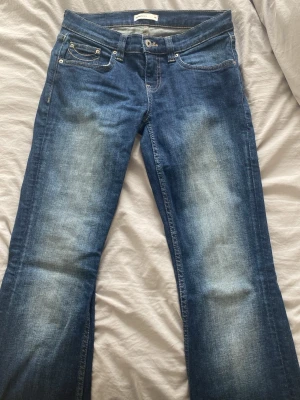 Blå bootcut jeans med kontrastsömmar - Säljer ett par klassiska blå bootcut jeans med snygga kontrastsömmar på bakfickorna och slitningar framtill. Jeansen har fem fickor och normal midja. Perfekta till vardagslooken och tillverkade i mjuk denim med lite stretch.