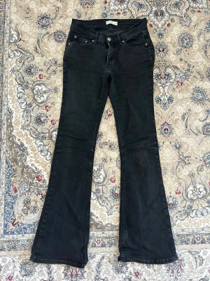 Svarta bootcut jeans med utsvängda ben - Säljer ett par svarta bootcut jeans med klassisk femficksmodell och utsvängda ben. Jeansen har knapp- och dragkedjestängning samt subtila slitningar för en cool look. Perfekta för dig som gillar retrovibbar och vill ha ett par jeans som sticker ut.
