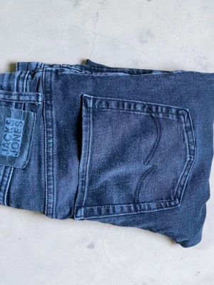 Mörkblå jeans från Jack & Jones - Snygga mörkblå jeans från Jack & Jones med klassisk femficksdesign och raka ben. Jeansen har en diskret tvättad look och är tillverkade i mjukt denimtyg som ger en skön passform. Perfekta för dig som gillar stilrena och tidlösa jeans.
