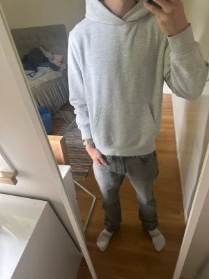 Ljusgrå basic hoodie med huva - En stilren ljusgrå hoodie med huva och magficka. Klassisk passform och ribbade muddar vid ärmar och nederkant. Perfekt för en avslappnad look och enkel att matcha med jeans eller joggers. Materialet känns mjukt och bekvämt.