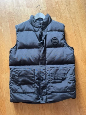Svart dunjacka från Canada Goose - Säljer en svart dunjacka från Canada Goose med klassisk design. Jackan har en slät yta, diskret innerfoder och detaljer som meshficka på insidan. Perfekt för kalla vinterdagar tack vare det varma dunfodret och den tåliga ytterytan. har också Canada goose påse