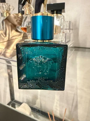 Versace Eros Eau de Toilette - Versace Eros Eau de Toilette i en lyxig turkosblå glasflaska med gulddetaljer och Medusa-huvud i relief på framsidan. Flaskan har en fyrkantig form och ett elegant, geometriskt mönster. Perfekt för dig som gillar exklusiva och stilrena dofter. över hälften kvar ( se sista bild ) 