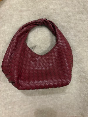 Vinröd väska, Gina tricot - Snygg vinröd handväska med flätad design och rundad form. Väskan är gjord i läder och har ett praktiskt handtag samt dragkedja upptill. Perfekt accessoar för att lyfta din outfit med en trendig touch. Köpt för 399kr❤️