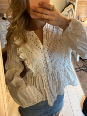 Vit broderad blus med volang - Supersöt vit blus med broderade blommor och hålbroderier framtill. 