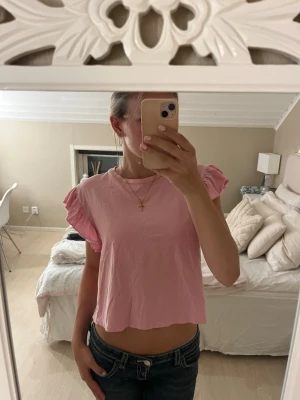 Topp med volangärmar - Söt rosa topp med korta volangärmar och rund hals. Toppen har en croppad passform och är tillverkad i mjuk bomull, perfekt för en avslappnad och trendig look💗