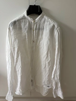 Vit linneskjorta med ståkrage - Säljer en vit skjorta i linne . En avslappnad passform, perfekt för en clean och stilren look. Finns ett nice märke nere vid midjan och en av knapparna är special designade med boomerang loggan! Skjortan ser ännu bättre ut om den stryks vilket den inte gjorts på bilden