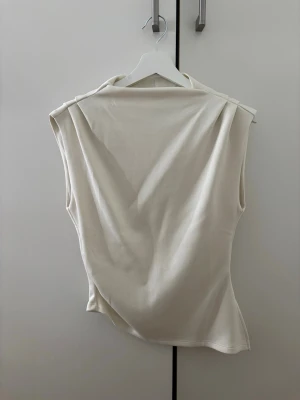 Vit ärmlös linnetopp - Stilren vit linnetopp med breda axlar och mjukt, följsamt material. Toppen är ärmlös och har en enkel, clean design som passar perfekt till många olika looks. Perfekt för dig som gillar minimalistisk stil.