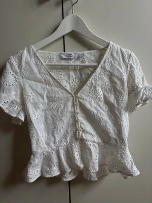 Vit blus med spets och volang - Söt vit sommar blus från & other stories med broderade blommor, v-ringning och knappar framtill. Kortärmad modell med volangkant nedtill och spetsdetaljer. 