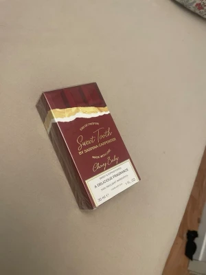 Sweet Tooth Cherry Baby parfym 30 ml - Sweet Tooth Cherry Baby är en Eau de Parfum från Sabrina Carpenter. Förpackningen är vinröd med gulddetaljer och har en chokladinspirerad design. Innehåller 30 ml och doften beskrivs som söt och gourmand med inslag av körsbär.