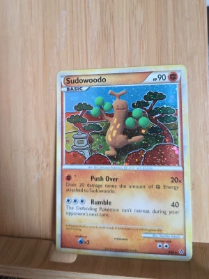 Pokémonkort Sudowoodo - Samlarobjekt! Pokémonkort med Sudowoodo-motiv. Kortet har färgglad framsida med illustration av Sudowoodo och text på engelska. Baksidan har klassisk blå Pokémon-design med Pokéboll. Perfekt till Pokémon-samlingen.