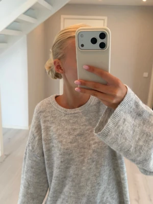 Ljusgrå stickad tröja - Mysig ljusgrå stickad tröja med oversized passform och rund halsringning. Tröjan har långa, vida ärmar och är tillverkad i ett mjukt material. Enkel och stilren design som är lätt att matcha.