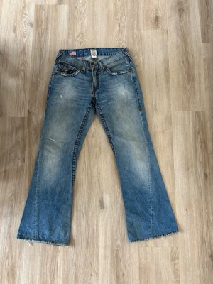 True Religion bootcut jeans ~ Joey Super T - Säljer dessa feta True Religion jeans i mycket bra skick. Storlek 31. Är en knapp som saknas så satt ditt en annan ( se bild 4) men är inget som syns vid användning. Hör av er vid frågor eller minsta fundering 🙌  Ytterbenslängd: 105 cm  Innerbenslängd: 75 cm  Midja: 38 cm  Benöppning: 25,5 cm