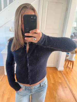 Mörkblå kofta - Mysig mörkblå kofta med fluffig textur och knappar framtill. Modellen är figurnära med långa ärmar och rund hals. Perfekt att styla med jeans för en avslappnad look.