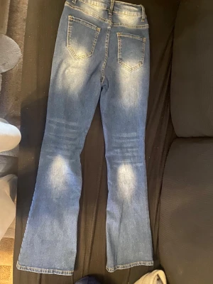 Blå bootcut jeans med slitningar - Ett par blå bootcut jeans med snygga slitningar och kontrastsömmar. Jeansen har fem fickor, bälteshällor och knappgylf. Tillverkade i klassisk denim med lite stretch för extra komfort.