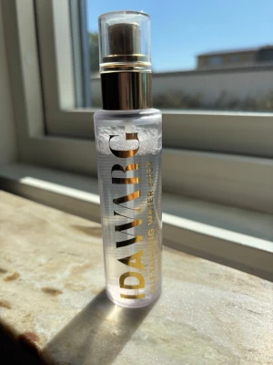 IDAWARG Self-Tanning Water Mist - Fräsch face mist från IDAWARG i genomskinlig plastflaska med guldfärgad text och spraymunstycke. Perfekt för att ge huden en naturlig solkysst look och återfukta ansiktet snabbt under dagen.