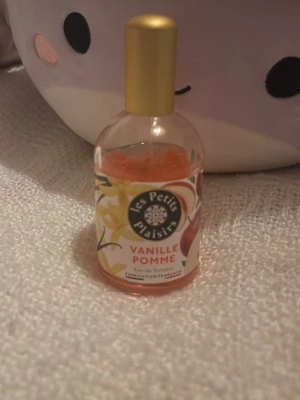 Les Petits Plaisirs Vanille Pomme parfym - En söt parfym från Les Petits Plaisirs med doft av vanilj och äpple. Flaskan är rund med guldfärgad kork och etikett med fruktmotiv. Innehållet är ljusrosa. Perfekt för dig som gillar fruktiga och söta dofter.