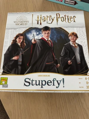 Harry Potter sällskapsspel Stupefy! - Säljer sällskapsspelet Stupefy! med Harry Potter-tema. Spelet har färgglada spelbrickor med elevhemmen Gryffindor, Slytherin och Ravenclaw samt kort och spelplan. Omslaget pryds av Harry, Hermione och Ron i sina Hogwarts-kläder. Perfekt för 4-8 spelare från 8 år.