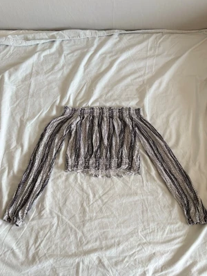 Off shoulder topp med mönster - Trendig off shoulder topp med långa ärmar. Toppen har ett svartvitt prickigt och randigt mönster, resår vid axlar och midja samt luftig passform. Perfekt för dig som gillar en bohemisk och avslappnad stil.