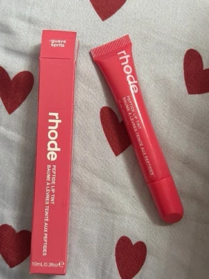 Rhode Peptide Lip Tint Guava Spritz - Rhode Peptide Lip Tint i färgen Guava Spritz. Läppbalsamet kommer i en rosa tub med vit text och matchande förpackning. Innehåller 10 ml och har en smidig applikator. Perfekt för dig som vill ha återfuktade och lätt färgade läppar.
