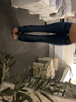 Mörkblå bootcut jeans - Säljer ett par mörkblå bootcut jeans med klassisk femficksdesign och låg midja. Jeansen har en snygg tvätt och raka ben som går ut lite nedtill. Perfekta för dig som gillar en tidlös och avslappnad stil. Ganska korta i modellen jag är 170 och de är lite korta 