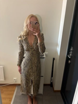 Adoore Paris dress Zebramönstrad - Snygg klänning från Adoore med zebramönster i beige och brunt. Klänningen har v-ringning, långa ärmar och knappar framtill hela vägen ner. Perfekt för dig som vill sticka ut med ett trendigt djurmönster. Finns inga defekter, som ny