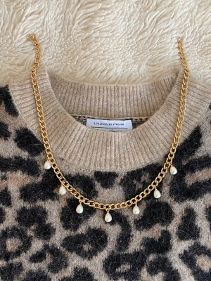Guldfärgat halsband med pärldroppar - Snyggt halsband i guldfärgad rostfritt med sju hängande droppformade pärlor. Kedjan är av klassisk modell och pärlorna ger en elegant touch. Perfekt accessoar för att lyfta din outfit med en trendig och stilren känsla.