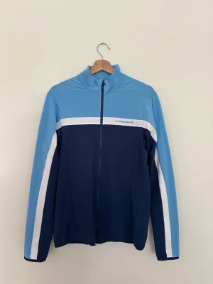 Blå träningsjacka från J.Lindeberg - Säljer en blå J.Lindeberg Jarvis Mid Layer med logotyp på bröstet. Perfekt som mellanlager för golf, träning eller vardag. Använd endast ett fåtal gånger och är i nyskick. Originalpris ca 1 290 kr. Skickas eller hämtas enligt överenskommelse.