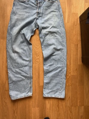 Baggy ljusblå jeans med raka ben - Säljer ett par baggy ljusblå jeans med raka ben och klassisk femficksdesign. Jeansen har hög midja och stängs med knappar. Perfekta för en avslappnad och trendig stil. Materialet är denim i 100% bomull.