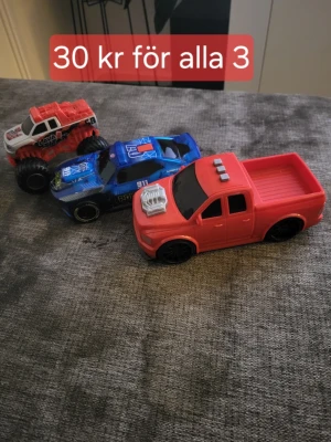 Tre leksaksbilar i plast - Säljer tre leksaksbilar i plast: en röd pickup, en blå polisbil och en rödvit monstertruck. Alla bilar har svarta hjul och detaljer som motorhuv och dekaler. Perfekt för dig som gillar att leka med bilar eller samla på små fordon. 2 av dom e me ljud. 