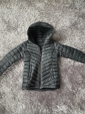 Svart dunjacka Peak Performance XS - Snygg svart dunjacka från Peak Performance i storlek XS. Jackan har huva, dragkedja framtill och quiltat mönster. Perfekt för kalla vinterdagar och riktigt lätt att bära. Klassisk och stilren design som passar till det mesta. Väldigt fint skick 