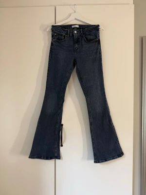 Mörkblå bootcut jeans - Säljer ett par mörkblå bootcut jeans med klassisk femficksdesign och hög midja. Jeansen har utsvängda ben och är tillverkade i ett mjukt denimtyg. Perfekta för dig som gillar retrovibbar och vill ha ett par snygga jeans med skön passform.