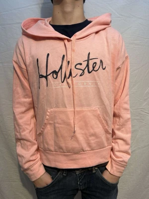 Ljusrosa vintage Hollister hoodie - Fet ljusrosa vintage hoodie med en snygg text framtill. Märke:Hollister! OBS UNISEX!! Size S. Skick9/10. Modellen är 164cm och väger 53kg!!!! Så den är mindre i storleken.