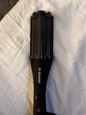 Svart vågtång från HH Simonsen - Säljer en svart vågtång från HH Simonsen med tre cylindrar för att skapa snygga vågor i håret. Ergonomiskt handtag och enkel knapp för låsning. Perfekt för dig som vill fixa håret snabbt och smidigt.
