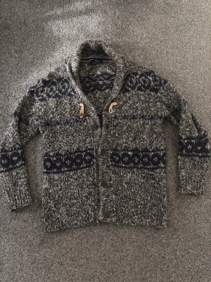 Grå Cardigan men blåa mönster  - Tjenare, säljer nu en fet grå Cardigan med blåa detaljer. Den är medium. Den är perfekt för dig som vill se bra ut i vinter. Den är varm också