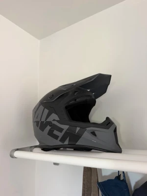 Svart och grå moppehjälm RAVEN - Säljer en snygg svart och grå crosshjälm från RAVEN med cool design och skärm framtill. Hjälmen har ventilationshål och vadderad insida för extra komfort. Perfekt för motocross eller offroad-äventyr.