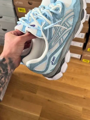  Nya ASICS blåvita sneakers - Snygga sneakers från ASICS i vitt och ljusblått med grå detaljer. Ovandelen är i mesh och mocka för en sportig vibe, och sulan är rejäl med bra grepp. Perfekta för dig som gillar streetstyle och bekväma skor.