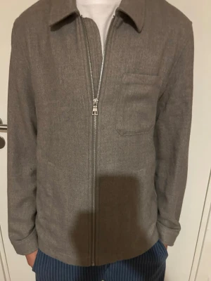 Gråbeige overshirt med dragkedja - Stilren gråbeige overshirt med rak passform, dragkedja framtill och en bröstficka. Klassisk krage och långa ärmar. Materialet ser ut att vara mjukt och något tjockare, perfekt för lager på lager. Använt den en gång. Enkel och clean design som passar till mycket.🙌💯, Storlek XS, priset kan även diskuteras.