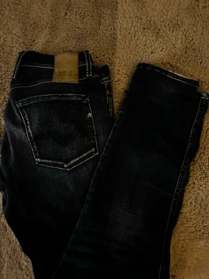 Mörkblå Replay Hyperflex jeans - Snygga mörkblå jeans från Replay Hyperflex med klassisk femficksdesign och kontrastsömmar. Jeansen har en skinnpatch bak i midjan och diskret Replay-logga på bakfickan. Materialet är stretchigt för extra komfort.