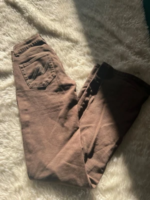 Bruna raka jeans med broderad ficka - Säljer ett par bruna jeans med rak passform och snygg broderad detalj på bakfickan. Jeansen har klassisk femficksdesign och är tillverkade i ett mjukt bomullstyg. Perfekta för dig som vill ha en chill och stilren look.