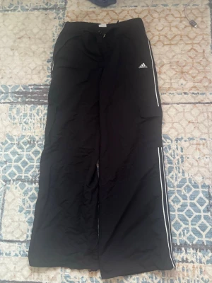 Svarta träningsbyxor från Adidas - Säljer ett par vintage Adidas-byxor 2003! Snygg Y2K-modell med cargoficka på benet, vita ränder och broderad logga. Lite slitage längst ner på ena benet men syns knappt!  
