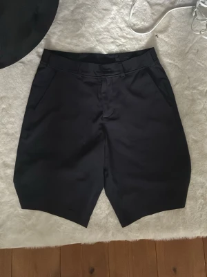 Svarta golf shorts ifrån bogey&birdies - Stilrena svarta shorts med midwaist passform och raka ben. Shortsen har fickor på sidorna och stängs med knapp och dragkedja. Perfekta för en clean och enkel look.