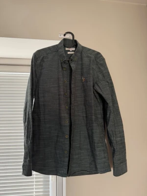 U.S Polo ASSN skjorta  - Snygg mörkgrå skjorta med diskret mönster och klassisk krage.  Passar till fest eller en avslappnad men stilren look. Skjortan är Storlek M och är väldigt lätt stylad. 