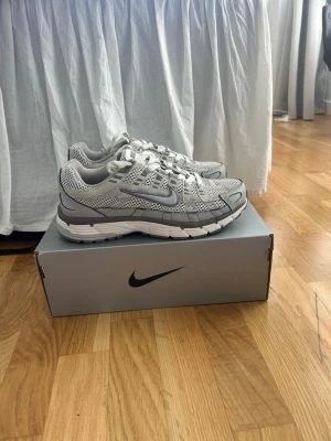 Nike gråvita Nike p-6000 - Snygga sneakers från Nike i grått och vitt med meshpaneler och detaljer i syntet. Skorna har en sportig vibe med tydlig swoosh-logga på sidan och robust sula. Perfekta för dig som gillar streetwear och vill ha bekväma skor till vardags.