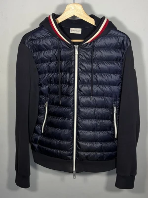 Maglia Cardigan - Mörkblå cardigan från Moncler i absolut toppskick. Storlek M fits S/M. Jackan har luva med de klassiska tricolor färgerna och snören.