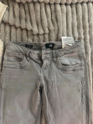 Grå jeans från LTB - Snygga grå jeans från LTB med klassisk femficksdesign och raka ben. Jeansen har silverfärgade nitar och knapp, samt diskreta sömmar på bakfickorna. Perfekta för en stilren och avslappnad look.