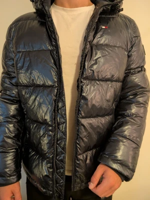 Tommy Hilfiger dunjacka marinblå, stl M - Tommy Hilfiger huvjacka i marinblått med Hilfiger-logga på bröstet och flaggan på ärmen. Stl M. Varm och praktisk för vintern, fint skick. Modell: 182cm | 83kg.